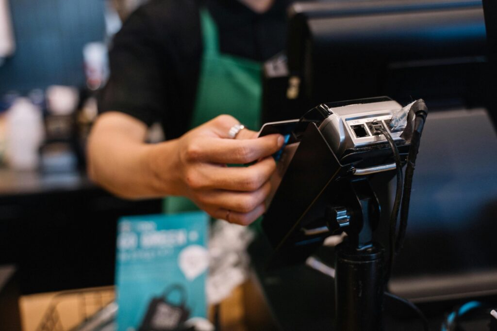 Barista in a green apron inserting a card into a payment terminal at a checkout counter