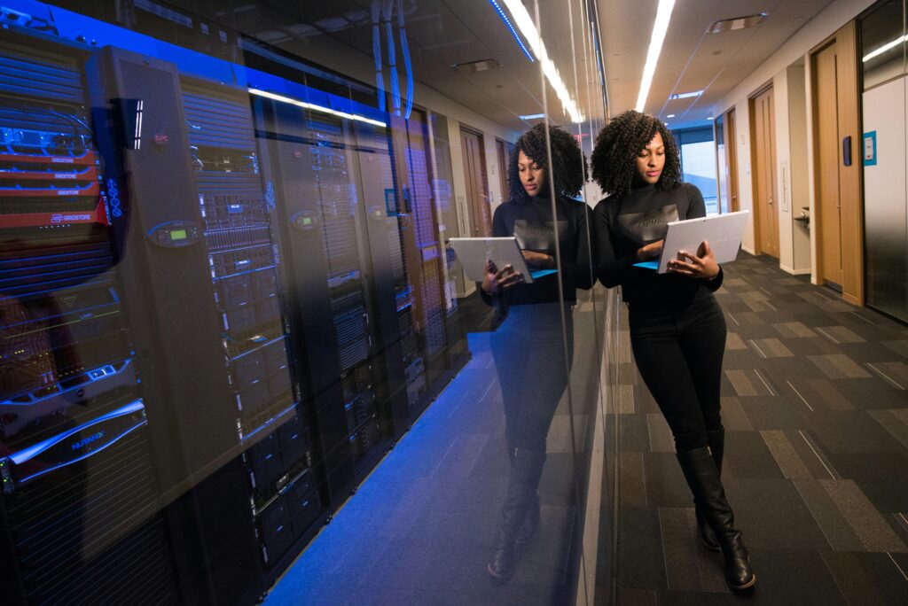Woman holding a laptop beside glass-walled server racks in a data centre corridor