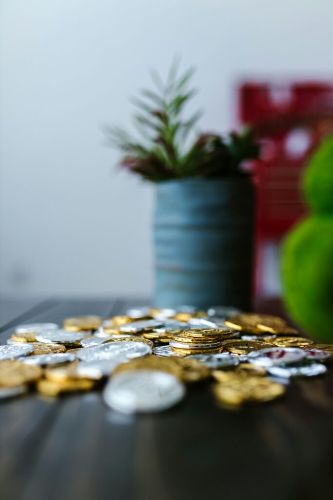 Gold and silver coins spread on a table beside a small potted plant