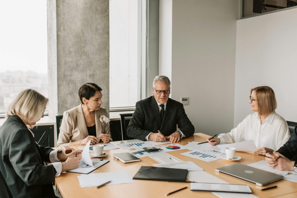Executives reviewing printed charts and reports around a conference table by a window