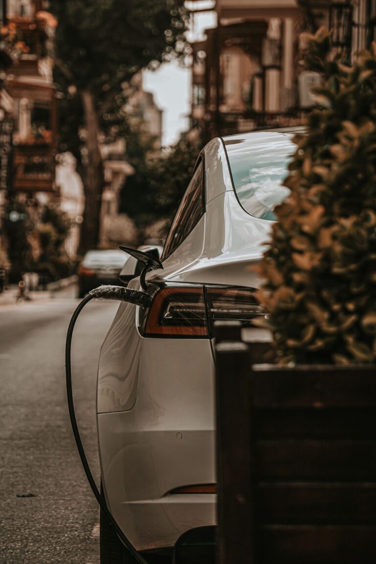 White electric car charging by cable on a tree-lined city street