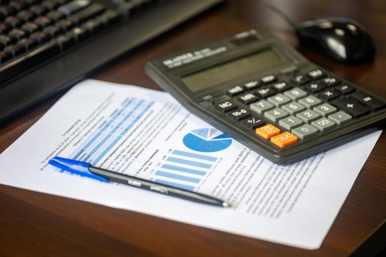 Desktop calculator and pen on a printed financial report with bar and pie charts